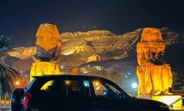 Black SUV parked at night in front of the illuminated Colossi of Memnon in Luxor, Egypt.