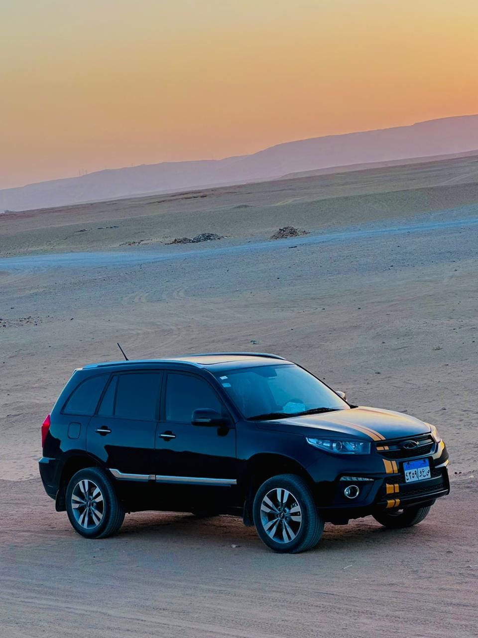 A black SUV with yellow racing stripes parked on desert terrain at sunset, showcasing Thutmoses Tours' adventurous desert excursions and travel experiences.