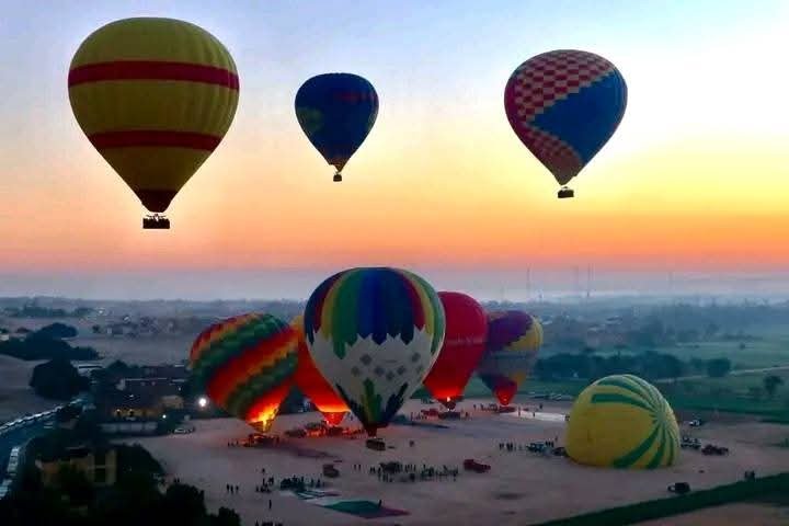 Hot air balloon flying over Luxor’s West Bank at sunrise, with temples and farmland below.